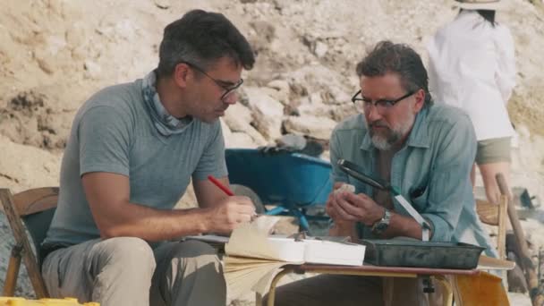 Arqueólogos do sexo masculino analisando achados durante a expedição — Vídeo de Stock