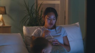 Asyalı anne TV karşısında yemek yiyor.