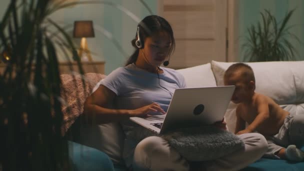Мати азіатського походження використовує ноутбук біля сина. — стокове відео