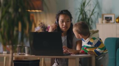 Asyalı anne çocuğun yanında video görüşmesi yapıyor.