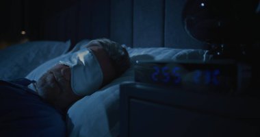 Yakın plan Orta yaşlı adam uykusuzluktan muzdarip. Gri saçlı adam, beyaz uyku maskesi takmış, yatakta uyanık yatıyor. Uykusuzluk, uykusuzluk, stres, gece anksiyetesiyle sessiz mücadele kavramını kabul et..