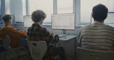 Programlama görevleri üzerinde çalışan bir grup genç üniversite öğrencisi. Parlak Bilgisayar Laboratuvarında Çocuklar Birlikte Kodlanıyor. Odaklanmış Öğrenciler Monitörler Üzerine Yazılım Geliştirme Üzerine Kod Yazıyor. Arka Görünüm.