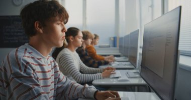 Çizgili Gömlekli Öğrencinin Kapanışı Yazma Koduna Yoğunlaşıyor. Oyun Tasarımı Projeleri üzerinde çalışan sınıf arkadaşlarıyla bilgisayar laboratuvarı. Modern eğitim ve gelecek bilişim becerileri kavramı. Sabit Çekim.