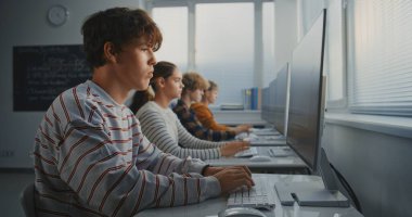 Sınıfta Oyun Geliştirme Görevi 'nde çalışan erkek öğrenci. Konsantre Genç Adam Ekran Üzerine Kod Yazarken, Sınıf Arkadaşları da Yazılım Programı Çalışıyor. Dijital Öğrenme ve Takım Çalışması. Sabit Çekim.