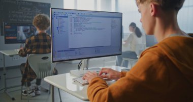 Orange Hoodie 'deki konsantre öğrenci bilgisayarda bilgisayar oyunu için kod yazıyor. Sınıftaki Genç Adam Oyun Mekaniği Oluşturdu. Oyun Geliştirme, Kodlama, Modern Dijital Eğitim kavramı. Sabit Çekim.