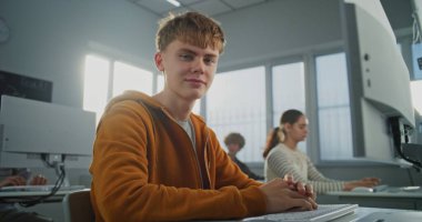 Turuncu Kapüşonlu Gülümseyen Öğrenci Oyun Geliştirme 'de çalışıyor. Genç Adam, Program ve Tasarım Öğrenirken Kameraya Bakıyor. Dijital Eğitim, Teknoloji ve Yaratıcı Yetenekler kavramı. Portre.