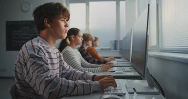 Sınıfta Oyun Geliştirme Görevi 'nde çalışan erkek öğrenci. Konsantre Genç Adam Ekran Üzerine Kod Yazarken, Sınıf Arkadaşları da Yazılım Programı Çalışıyor. Dijital Öğrenme ve Takım Çalışması. Sabit Çekim.