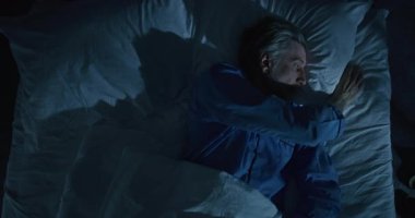 Yataktaki Adam, Soğuk Ay Işığıyla Aydınlanan Uykusuzluk Çeken Adam. Avrupalı Adam, Yorgun ve Sinirli, İpek Uyku Maskesi Takıyor. Uykusuzluk, uykusuzluk, akıl sağlığı. Üst Manzara. Sabit Çekim.