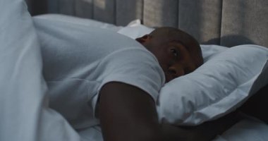 African American Man Slowly Wakes Up With Pleasure in Soft Bed, Full of Fresh Energy. Adult Man Wakes Up in Good Mood. Concept of Healthy Sleep, Good Morning, Energy After Rest. Static Shot.