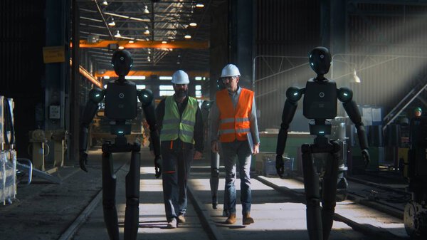 Инженеры в защитных жилетах и шлемах сотрудничают с гуманоидными роботами внутри высокотехнологичного промышленного комплекса. Будущее смарт-производства Бесшовная работа робота человека в команде, инновации в производстве.