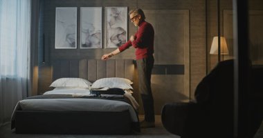 Kırmızı balıkçı yakalı gri saçlı adam ait olduğu eşyaları Stylish Otel odasındaki çantaya koyar. Gezgin Rutini, Seyahat Hazırlığı, İş Yaşamı, Anlık Düzenleme ve Odaklanma Konsepti.