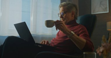 Stylish Otel 'de dizüstü bilgisayarda çalışırken Kırmızı Balıkçı yaka giyen modern işadamı kahve ve kahvaltıdan zevk alıyor. Gevşek Üretim, Seyahat, Profesyonel Yaşam Tarzı, Konforlu İş Seyahati kavramı.