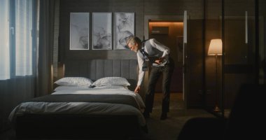 Resmi Takım Elbiseli Otel Yöneticisi Tablet Fotoğrafı kullanarak Lüks Otel Odasını Denetliyor ve Yatak Düzenlemesini Değerlendiriyor. Konukseverlik Standartları, Kalite Kontrolü, Profesyonel Yönetim.