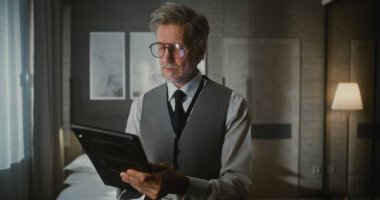 Yelek ve Kravat Giyen Gri Saçlı Adam, Dijital Tablet veya İnce Dizüstü Bilgisayarlı Ellere Bakıyor. Uzaktan Yönetim, Dijital Profesyonellik, Mobil Teknoloji, İş Seyahati. Portre.