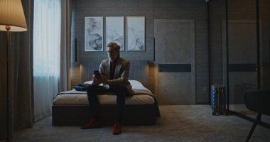 Tarz sahibi gri saçlı adam modern otel odasına yerleşti. İş adamı hemen cevapsız arama ve mesajları kontrol eder. Konsept İş Gezileri, Otel Kalışları, Modern İşlerin Dijital Düzenlemesi.