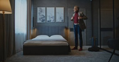 Yakışıklı Olgun Adam Modern Otel Odası 'na yerleşti. İş adamı ceketini çıkardı ve Yorgun bir şekilde yatağa uzandı. İş gezisi kavramı, otelde kalmak ve yolculuktan sonra dinlenmek. Sabit Çekim.