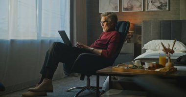 Odaklanmış İşadamı, otel odasının Sabah Işığı 'nda dizüstü bilgisayarda çalışıyor. 