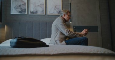 Yorgun Adam Akıllı Telefon Kontrol Sosyal Medyasına ulaşmadan önce çantasını bırakıyor. Modern Gerçeklik Dijital Alışkanlıkları kavramı, Yeni veya Tanıdık Uzayda Dijital Konfor Arayışı. El bilgisayarı.