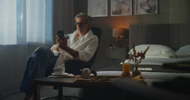 Soft White Bornoz 'daki son sınıf öğrencisi internetten akıllı telefon kullanıp ödemeleri yönetiyor. Otel odasında sakin bir sabah. Dijital Konfor, Özgürlük ve Seyahat Yaşam Tarzı kavramı. Doli Vuruşu.