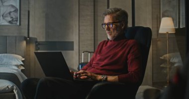 Modern Otel 'de gece geç saatlere kadar çalışan profesyonel, yakışıklı adam lambayla aydınlatılıyor. Adam tamamen işe odaklanmış. Konsept İş Gezisi, Teknoloji ve Sessiz Üretim. Sabit Çekim.