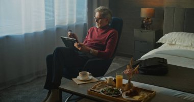 Stylish Otel 'deki Olgun Adam Tablet' teki Online Store 'a bakarken Sabah Kahvaltısının keyfini çıkarıyor. Uzaktan Çalışma, Dijital Yaşam Tarzı, Çevrimiçi Alışveriş ve İş Seyahatleri rutinini hesaba katın. Sabit Çekim.