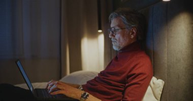 Yorgun İşadamı otel yatağında yatarken kişisel bilgisayarda çalışıyor. Akşam, Otel Odası 'nda, Laptop Klavyesinde Erkek Tipleri. Uzaktan Çalışma Konsepti, Gece Verimliliği, İş Hayatı.