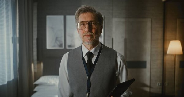 Портрет руководителя в современном гостиничном номере. Зрелый человек в жилете и галстуке стоит с серьезным, уверенным выражением с гаджетом в руках. Концепция современного исполнительного, делового профессионализма.