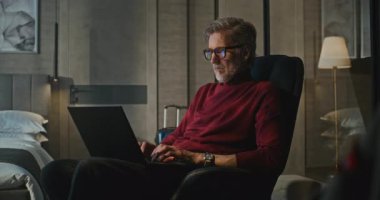 Modern Otel 'de gece geç saatlere kadar çalışan profesyonel, yakışıklı adam lambayla aydınlatılıyor. Adam tamamen işe odaklanmış. Konsept İş Gezisi, Teknoloji ve Sessiz Üretim. Sabit Çekim.