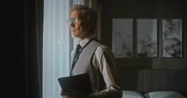 Sunum için Sunucu Sunny Otel Odasında. Kendine güveni tam bir işadamı, elinde dijital tabletle pencerenin önünde toplanmaya hazır bekliyor. Profesyonel Eğitim, Dijital Çalışma Akışı. Portre.