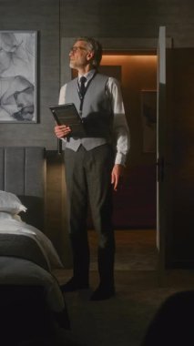 Profesyonel İş Giysileri ve Fotoğrafları Titizlikle Düzenleyen Yetişkin Otel Müdürü Lüks Otel Odasında Tabletle Kusursuz Bir Yatak Yaptı. Kalite Kontrol ve Oda Hazırlığı. Dikey Çekim.