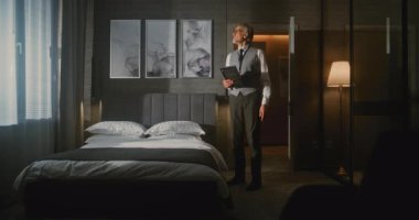 Profesyonel İş Giysileri ve Fotoğrafları Titizlikle Düzenleyen Yetişkin Otel Müdürü Lüks Otel Odasında Tabletle Kusursuz Bir Yatak Yaptı. Kalite Kontrol ve Oda Hazırlığı. Sabit Çekim.