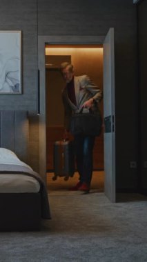 Tarz sahibi gri saçlı adam modern otel odasına yerleşti. İş adamı hemen cevapsız arama ve mesajları kontrol eder. Konsept iş seyahatleri, Hotel Stays, Dijital rutin. Dikey Çekim.