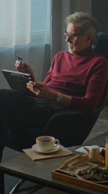 Stylish Otel 'deki Olgun Adam Tablet' teki Online Store 'a bakarken Sabah Kahvaltısının keyfini çıkarıyor. Uzaktan Çalışma, Dijital Yaşam Tarzı, Çevrimiçi Alışveriş ve İş Seyahatleri rutinini hesaba katın. Dikey Çekim.