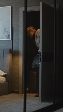 Entellektüel Gri Saçlı İşadamı Otel Odasına Geldi, Arama ve E-postaları Anlık Kontrol Etti. Modern Business Travel, Constant Connectivity ve Digital Lifestyle kavramları. Dikey Çekim.