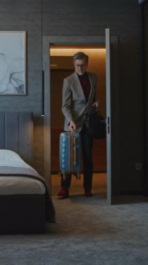 Yakışıklı Olgun Adam Modern Otel Odası 'na yerleşti. İş adamı ceketini çıkardı ve Yorgun bir şekilde yatağa uzandı. İş gezisi kavramı, otelde kalmak ve yolculuktan sonra dinlenmek. Dikey Çekim.