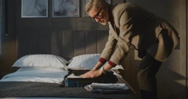 Zarif gri saçlı adam titizlikle giysilerini küçük mavi bavula koyar. Uçağa yetişmek için aceleyle otelden ayrılan adam. Seyahat kavramı, Gezgin Rutini, İş Gezisi. Sabit Çekim.