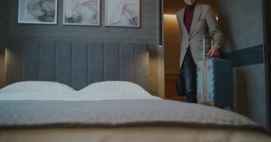 Yorgun adam odaya giriyor. Eşyaları açmadan, Adam anında telefon alışkanlığını kontrol edip sosyal medyayı kontrol ediyor. Seyahat, Konfor, Modern Yaşam Tarzı ve Dijital Alışkanlıklardan Yorgunluk kavramı. El bilgisayarı.