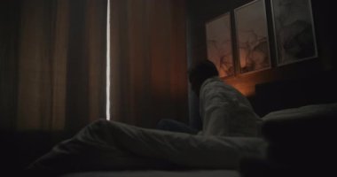 Modern Otel Odasında Yeni Gün 'e Hoş Geldiniz. Pijama ve bornoz giyen adam, güneşli pencereden dışarı bakarken yataktan çıkar ve gerilir. Rahatlama kavramı, seyahat ederken, duygusal refah....