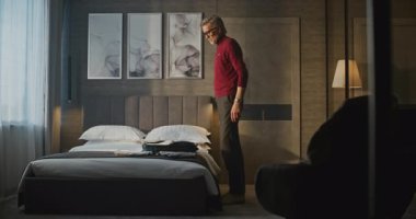 Kırmızı balıkçı yakalı gri saçlı adam ait olduğu eşyaları Stylish Otel odasındaki çantaya koyar. Gezgin Rutini, Seyahat Hazırlığı, İş Yaşamı, Anlık Düzenleme ve Odaklanma Konsepti.