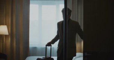 Olgun bir iş adamı, uzun bir iş seyahatinden sonra şık bir otel odasına girer. Yorgun ama rahatlamış, Erkek ceketini çıkarıp beyaz yatağa uzanıyor. Seyahat Yorgunluğu, Rahatlık ve Modern Yaşam Tarzı kavramı.