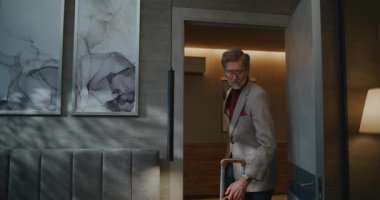 Gri saçlı adam zor bir yolculuktan sonra iş gezisine çıktı. Güneşli otel odasına giriş yaptı. Giysiler içindeki adam yatağa uzanır, gözleri ovalar ve alnını sıvazlar, sanki başı ağrıyormuş gibi. Doli Vuruşu.