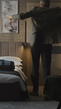 Yakışıklı Olgun Adam Bavula Ait Paketler, Ceketini Giyer ve Otel Odasından Çıkıyor. Seyahat rutini konsepti, seyahat hazırlığı, iş hayatı, iş seyahatleri. Dikey Çekim.