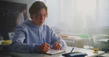 Mavi Kapüşonlu Genç, Masada Tek Başına Oturuyor, Düşüncede Kaybolan Kadın Sınıf Arkadaşı Sessizce Yürüyen Elma Çekirdeğini Masada Bırakıyor. Kavramsal Yalnızlık, Sessiz Bağlantı ve Duygusal Mesafe.