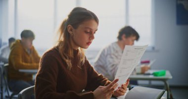 Genç Bayan Öğrenci Sınav Raporu Olarak Parlak Gülümsüyor ya da Parlak Sınıfta Masada Otururken Başarılı Sınav Kağıdı. Akademik Başarı Kavramları, Öğrenci Başarı, Öğrenim Keyfi.