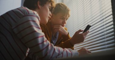 Parlak Sınıfın Pencere Altındaki Genç Çocuklar Telefonla Kaydırma, Sessiz Yorumlar Karşılıklı. Gençlik Kültürü Teknolojisi, Gelişigüzel İletişim, Olumlu Duygular ve Arkadaşlık Anları.