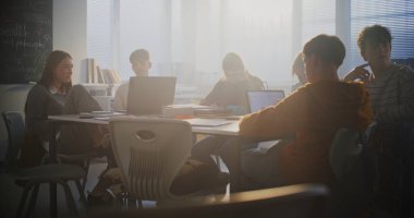 Çeşitli Öğrenci Grubu Merkez Masa etrafında toplanıp yoğun bir şekilde dizüstü bilgisayarlar üzerinde çalışıyor. İşbirliği, Grup Proje Çalışması ve Modern Eğitim Ayarlarında Dijital Öğrenmenin Temel Rolü.