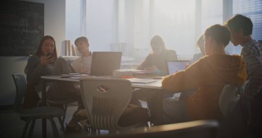 Çeşitli Öğrenci Grubu Merkez Masa etrafında toplanıp yoğun bir şekilde dizüstü bilgisayarlar üzerinde çalışıyor. İşbirliği, Grup Proje Çalışması ve Modern Eğitim Ayarlarında Dijital Öğrenmenin Temel Rolü.