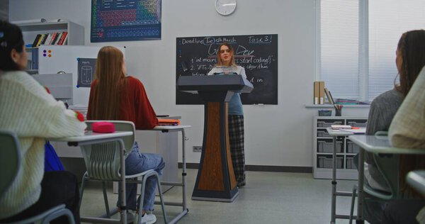 Молодая женщина уверенно говорит на подиуме, улыбаясь, обращаясь к одноклассникам и учителю. Концепция лидерства, уверенности и роста коммуникационных навыков через современное образование. Долли Шот.