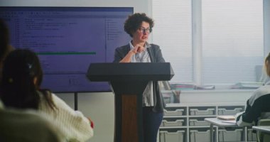 Kadın Kodlama Öğretmeni Podyumda Büyük Sayısal Ekranda Söz Dizimini Açıklıyor. Modern Bilgisayar Bilimi Eğitimi, BTMM Öğrenme, Teknoloji Edebiyatı ve Öğretim Yeniliği kavramını benimse.