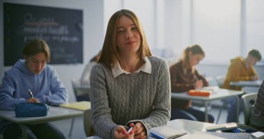 Açık, Dostane Gülümseyen ve Diş telleri Sınıfta Oturan Kız. Arka planda okuyan diğer öğrenciler. Öğrenci Özgüveni, Dostluk, Eğitimde Pozitif Öğrenme Ortamı. Portre.